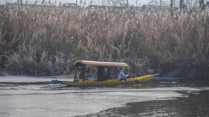 A Kashmiri boatman moves his boat through the frozen surface water of Dal Lake on a cold morning in  Srinagar, Indian controlled Kashmir, Wednesday, Jan. 4 , 2022. (AP Photo/Mukhtar Khan)