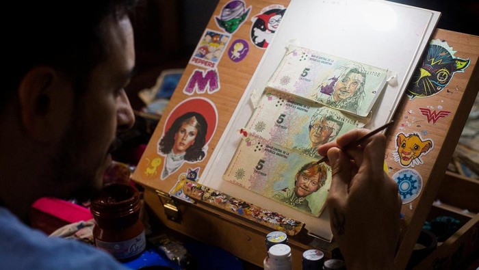 Artist Sergio Diaz holds intervened Argentine pesos bills and a US dollar depicting Steven Spielberg's movie 