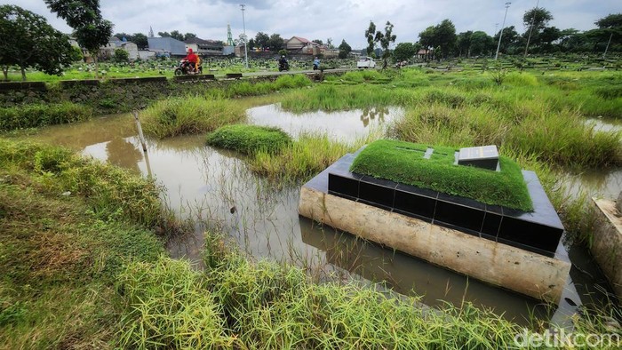 Warga melintas di jalan yang membelah kompleks TPU Tanah Kusir, Jakarta Selatan, Kamis (5/1/2023). Sebagian pemakaman masih tergenang air hujan pada Rabu (4/1). Cuaca ekstrim pada satu pekan terakhir membuat sejumlah titik tergenang seperti terlihat di TPU Tanah Kusir ini.