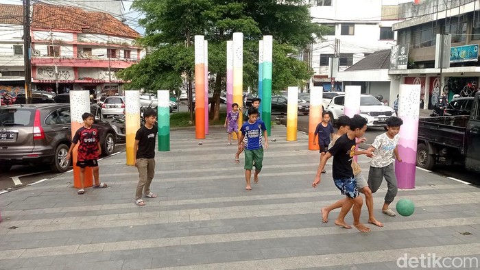 Anak-anak bermain bola di taman dekat jalanan.