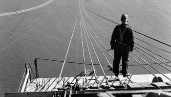 Seorang pria berdiri di kabel pertama selama pembangunan Jembatan Golden Gate, dengan Presidio dan San Francisco di latar belakang.1935 Foto: Instagram/The History Atlas 