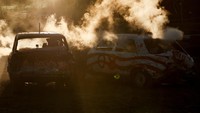 Pengemudi keluar dari mobilnya yang berselimut asap saat bersaing dalam kompetisi menghancurkan mobil bertajuk Demolition Derby.