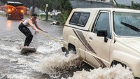 Papan selancar yang ditarik sebuah mobil itu menyusuri jalanan yang kebanjiran.