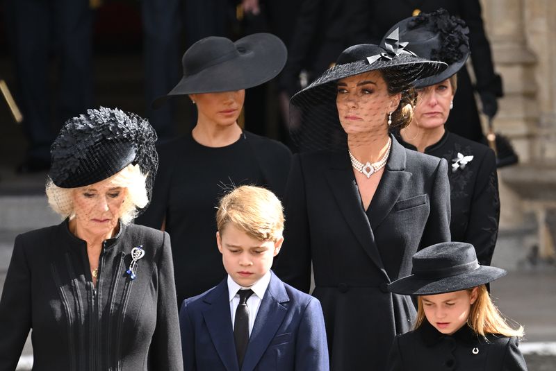 Meghan Markle vs Kate Middleton LONDON, ENGLAND - SEPTEMBER 19: (L-R) Camilla, Queen Consort, Meghan, Duchess of Sussex, Prince George of Wales, Catherine, Princess of Wales, Princess Charlotte of Wales and Sophie, Countess of Wessex during the State Funeral of Queen Elizabeth II at Westminster Abbey on September 19, 2022 in London, England. Elizabeth Alexandra Mary Windsor was born in Bruton Street, Mayfair, London on 21 April 1926. She married Prince Philip in 1947 and ascended the throne of the United Kingdom and Commonwealth on 6 February 1952 after the death of her Father, King George VI. Queen Elizabeth II died at Balmoral Castle in Scotland on September 8, 2022, and is succeeded by her eldest son, King Charles III. (Photo by Karwai Tang/WireImage)
