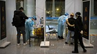 Pekerja yang mengenakan pakaian pelindung berdiri di bilik untuk menjalani tes COVID-19 bagi pelancong yang tiba di area kedatangan internasional di Bandara Internasional Ibukota Beijing.  