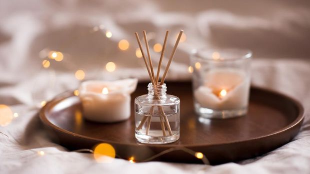 Home perfume in glass bottle with wood sticks, scented burn candles  tray in bedroom close up. Aromatherapy cozy atmosphere lifestyle. Winter warm xmas season.