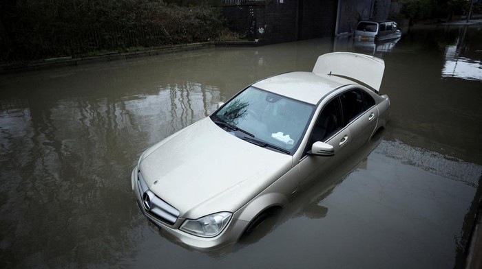 A woman walks down the street as a car is left partially submerged in water after heavy rain flooded a section of road in Stockport, Britain January 10, 2023. REUTERS/Phil Noble