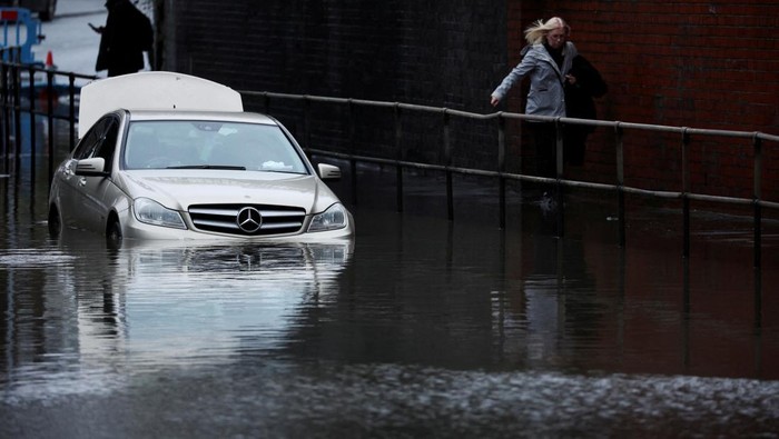 A woman walks down the street as a car is left partially submerged in water after heavy rain flooded a section of road in Stockport, Britain January 10, 2023. REUTERS/Phil Noble