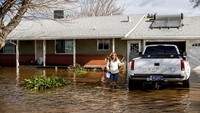 Kim Ochoa meninggalkan rumah dan mobilnya di Merced, California, yang dikelilingi banjir, saat badai terus melanda negara bagian itu. Badai itu didukung oleh dua fenomena yang tumpang tindih - aliran udara yang sangat besar dari uap air yang padat dari lautan yang disebut sungai atmosfer, dan sistem tekanan rendah yang dikenal sebagai siklon bom. AP/Noah Berger