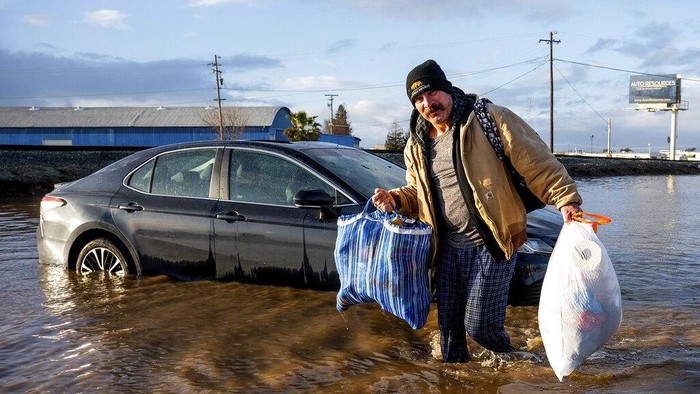 Mobil-mobil Jadi Korban Dahsyatnya Badai yang Menerjang California Jesus Torres carries belongings from his flooded Merced, Calif., home on Tuesday, Jan. 10, 2023. (AP Photo/Noah Berger)