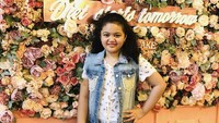 Mampir ke kafe kue kekinian, Amora tak lewatkan pose di spot Instagramable. Posenya tak kalah manis dengan bunga di belakangnya ya?