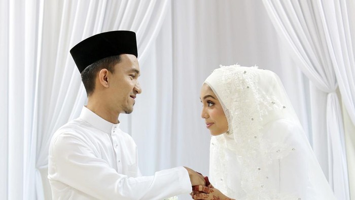 A Muslim young woman holding a young mans hand for salam (gesture of mannerism in greeting) when they are certified newlywed in Islam akad nikah (solemnisation) ceremony. In this ceremony, newlywed and all guests are required to wear pure white tradiitonal clothing.