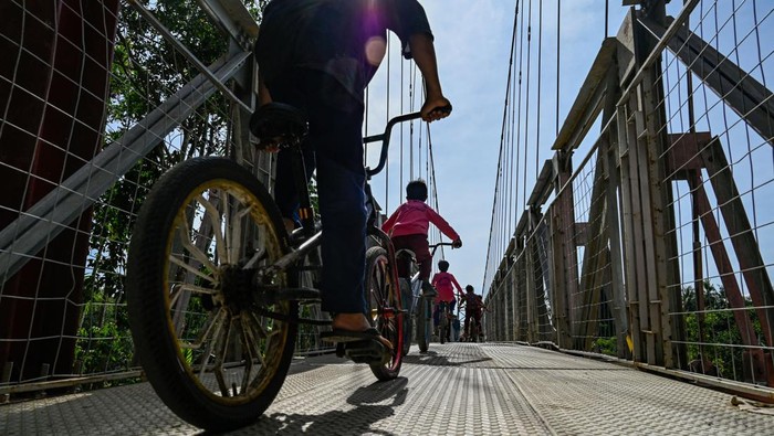 A woman and child walk past a newly-constructed suspension bridge across a river which residents previously crossed using rafts or waded through, in Siron village in Kuta Cot Glie, Aceh province on January 11, 2023. (Photo by CHAIDEER MAHYUDDIN / AFP) (Photo by CHAIDEER MAHYUDDIN/AFP via Getty Images)