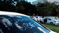 Tulisan Uber Out juga tertera di sebuah kaca mobil.