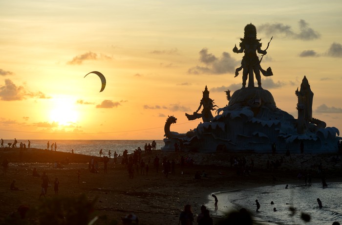 Wisatawan menikmati pemandangan matahari terbenam dari dekat Patung Triratna Amreta Bhuwana di kawasan wisata Pantai Jerman, Kuta, Badung, Bali, Kamis (12/1/2023). Patung Triratna Amreta Bhuwana yang baru selesai pembangunannya sebagai bagian dari proyek penataan Pantai Seminyak, Legian, Kuta (Samigita) itu dibangun sebagai ikon pariwisata baru untuk menarik kunjungan wisatawan ke Pantai Jerman. ANTARA FOTO/Fikri Yusuf/aww.