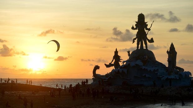 Wisatawan menikmati pemandangan matahari terbenam dari dekat Patung Triratna Amreta Bhuwana di kawasan wisata Pantai Jerman, Kuta, Badung, Bali, Kamis (12/1/2023). Patung Triratna Amreta Bhuwana yang baru selesai pembangunannya sebagai bagian dari proyek penataan Pantai Seminyak, Legian, Kuta (Samigita) itu dibangun sebagai ikon pariwisata baru untuk menarik kunjungan wisatawan ke Pantai Jerman. ANTARA FOTO/Fikri Yusuf/aww.