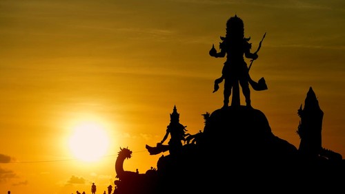 Wisatawan menikmati pemandangan matahari terbenam dari dekat Patung Triratna Amreta Bhuwana di kawasan wisata Pantai Jerman, Kuta, Badung, Bali, Kamis (12/1/2023). Patung Triratna Amreta Bhuwana yang baru selesai pembangunannya sebagai bagian dari proyek penataan Pantai Seminyak, Legian, Kuta (Samigita) itu dibangun sebagai ikon pariwisata baru untuk menarik kunjungan wisatawan ke Pantai Jerman. ANTARA FOTO/Fikri Yusuf/aww.