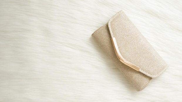 Shiny, golden clutch bag on white fluffy fur background. Woman accessory. Empty place for text. Closeup. Top down view.