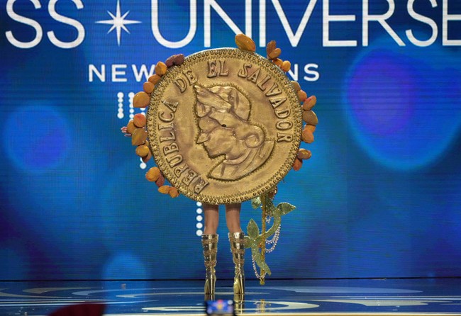 Aksesori Bitcoin raksasa berwarna emas disematkan di bagian punggung Miss Universe El Salvador 2022 Alejandra Guajardo. Ada juga detail biji cokelat di busana yang dipakai Alejandra. Bitcoin yang ditempelkan di busana Alejandra itu merupakan buatan seniman Francisco Guerrero. Foto: Getty Images