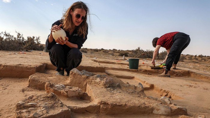 Potret Penemuan Telur Berusia 4.000 Tahun di Perbatasan Israel-Mesir Lauren Davis, excavation manager of the southern district at the Israel Antiquities Authority (IAA), shows a fresh ostrich egg used for illustration next to older egg fragments dating over 4000 years old next to an ancient fire pit at a site in the dunes near Nitzana along the Israel-Egypt border in the western Negev desert on January 12, 2023. - Experts say the finds provide insight into the life of the ancient peoples inhabiting the region. The eight crushed eggs were located at a camp site used by nomads