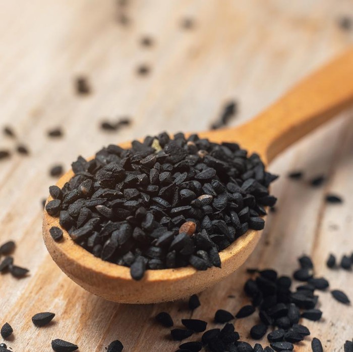 Black cumin seeds on wooden spoon on wooden background.