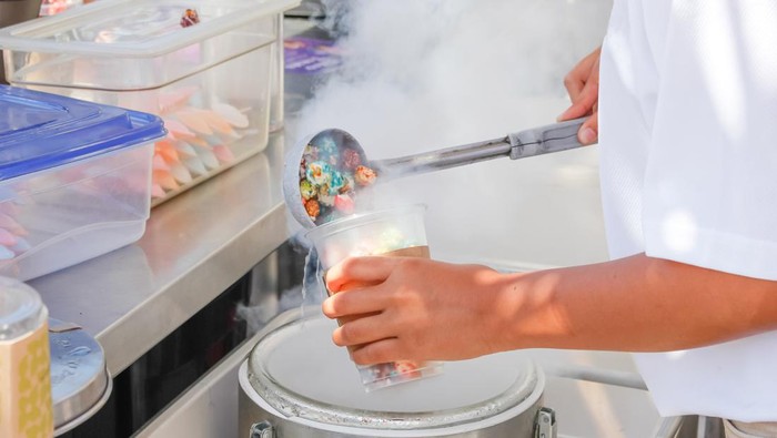 A view of an employee preparing a cup of dragons breath cereal dessert at a food stand.