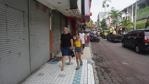 Wisatawan berjalan di kawasan pertokoan Kuta Square yang kini sepi karena banyak toko tutup.