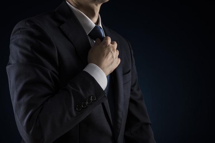 Businessman tightens tie. Over black background.