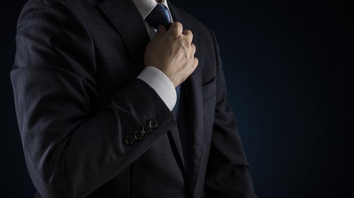 Businessman tightens tie. Over black background.