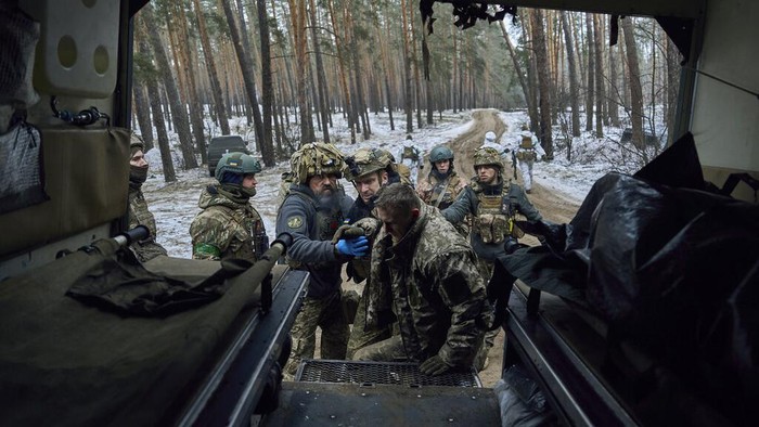 Military medics give first aid to a wounded soldier, right, and place the a body of a killed soldier into a bag, near Kremenna in the Luhansk region, Ukraine, Monday, Jan. 16, 2023. (AP Photo/LIBKOS)