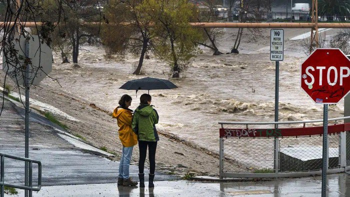 People watch the high volume of storm rain water flowing downstream at the Los Angeles River in Los Angeles on Saturday, Jan. 14, 2023. Storm-battered California got more wind, rain and snow on Saturday, raising flooding concerns, causing power outages and making travel dangerous. (AP Photo/Damian Dovarganes)