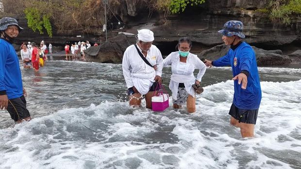 Petugas Satpolair Polres Tabanan dan life guard DTW Tanah Lot membantu menyeberangkan pemangku, pengempon, srati, dan pemedek yang hendak melakukan persembahyangan saat piodalan di Pura Luhur Tanah Lot, Rabu (18/1/2023).