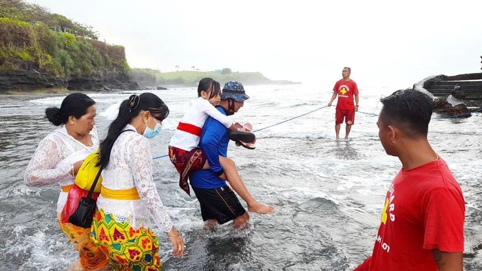 Petugas Satpolair Polres Tabanan dan life guard DTW Tanah Lot membantu menyeberangkan pemangku, pengempon, srati, dan pemedek yang hendak melakukan persembahyangan saat piodalan di Pura Luhur Tanah Lot, Rabu (18/1/2023). (istimewa)