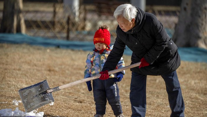 A child watches as an adult shovels snow at a public park in Beijing, Tuesday, Jan. 17, 2023. China has announced its first population decline in decades as what has been the worlds most populous nation ages and its birthrate plunges. (AP Photo/Mark Schiefelbein)
