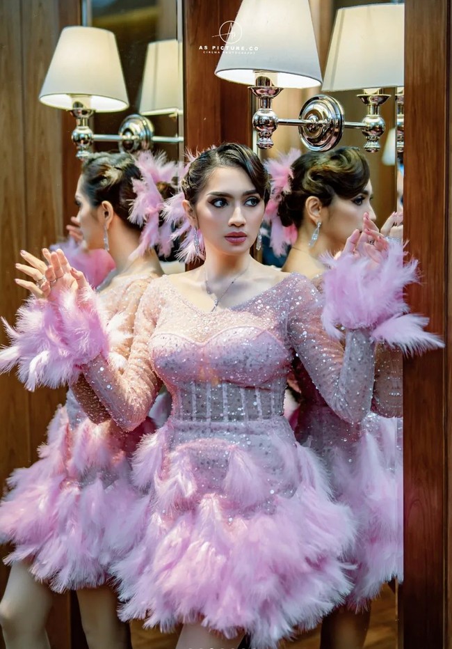 Untuk mempercantik penampilannya, Angel mengenakan riasan cukup tebal pada bagian matanya dengan eyeliner berbentuk cat eye. Rambutnya pun ditata rapi dicepol ke belakang dan dihiasi debgan bulu berwarna merah muda seperti yang ada di gaun yang dikenakannya. Foto: Instagram/@as_picture.co