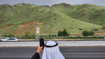Seorang warga mengambil foto sebuah bukit yang berubah menjadi hijau setelah hujan lebat di Mekkah, Arab Saudi pada 16 Januari 2023. Foto: Hani Alshaer/Anadolu Agency via Getty Images