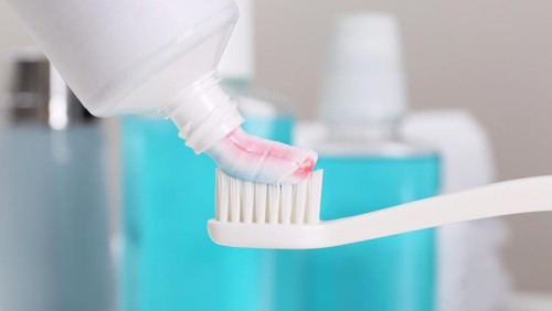 Applying paste on toothbrush near mouthwash, closeup