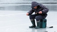 Pria itu memancing melalui lubang di aliran sungai yang membeku.