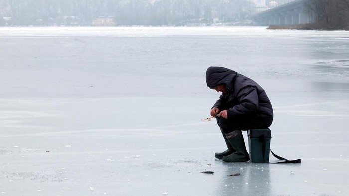 Mancing di Sungai Dnipro yang Membeku Seorang warga sedang memancing di Sungai Dnipro, Kyiv, yang membeku. Dia asyik mancing meski perang Rusia dan Ukraina masih berlanjut.