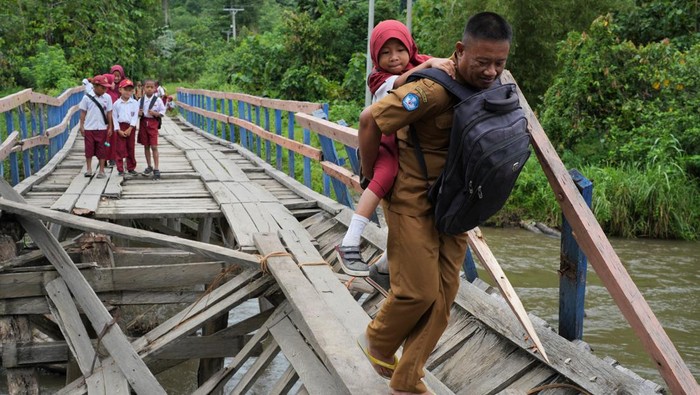 Seorang guru menggendong siswa SD Negeri 1 Alaaha saat menyeberangi jembatan rusak di Desa Alaaha, Kecamatan Ueesai, Kolaka Timur, Sulawesi Tenggara, Sabtu (21/1/2023). Jembatan yang menjadi akses satu-satunya dan penghubung tiga desa tersebut rusak akibat lapuk serta dorongan arus deras sungai Wandolaki sehingga menyebabkan sekitar 1.850 jiwa diwilayah tersebut tidak bisa beraktivitas normal. ANTARA FOTO/Jojon/YU