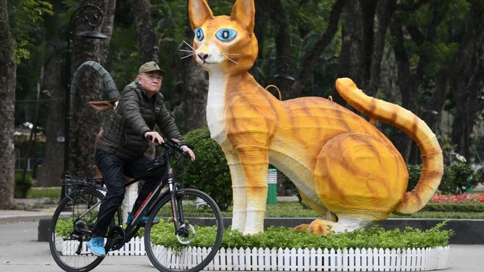 This photograph taken on January 16, 2023 shows a man riding a bicycle past a cat statue at Thong Nhat Park in Hanoi, ahead of the lunar new year. - As China gears up to welcome the Year of the Rabbit, the lunar new year looks slightly different in Vietnam -- where the Year of the Cat is about to begin. (Photo by Nhac NGUYEN / AFP) (Photo by NHAC NGUYEN/AFP via Getty Images)