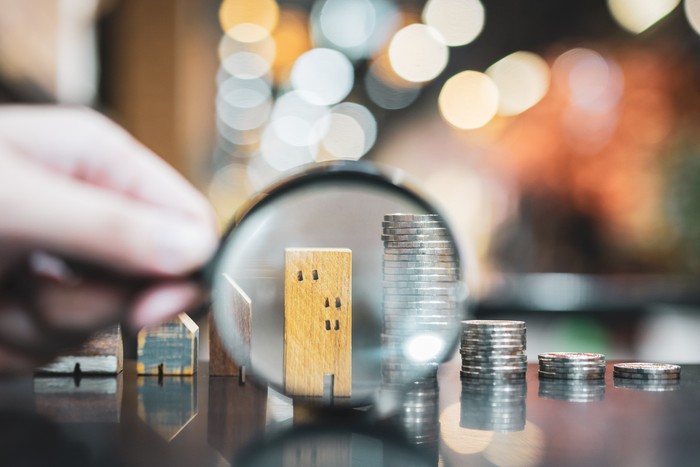 Hand holding magnifying glass and looking at house model, house selection, real estate concept.