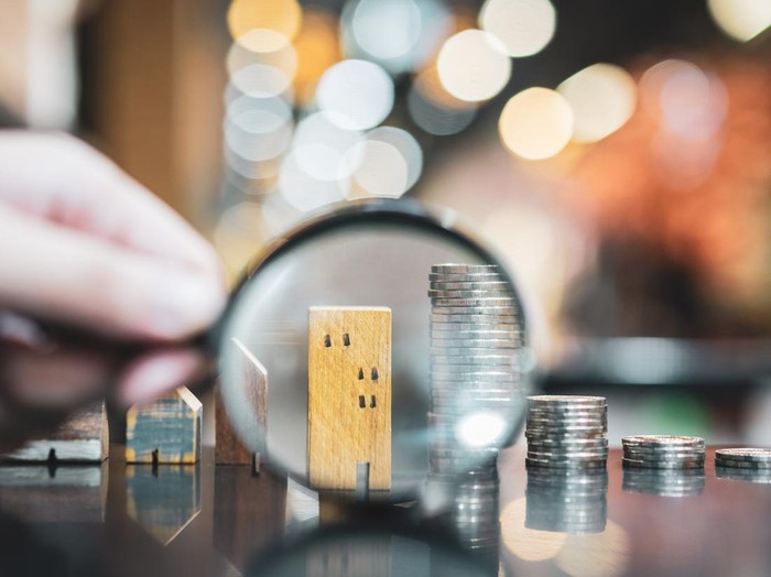 Hand holding magnifying glass and looking at house model, house selection, real estate concept.