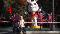 Seorang pria dan anak kecil berfoto di depan patung kelinci di sebuah taman.