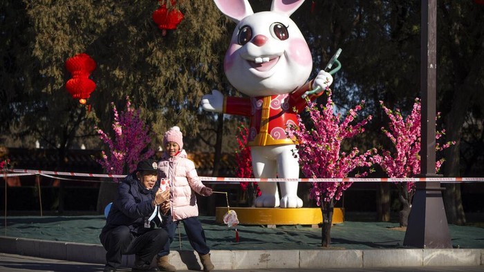 People walk along a path decorated with lanterns for the upcoming Lunar New Year at a public park in Beijing, Friday, Jan. 20, 2023. The Year of the Rabbit officially begins on Jan. 22. (AP Photo/Mark Schiefelbein)