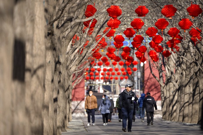 People walk along a path decorated with lanterns for the upcoming Lunar New Year at a public park in Beijing, Friday, Jan. 20, 2023. The Year of the Rabbit officially begins on Jan. 22. (AP Photo/Mark Schiefelbein)