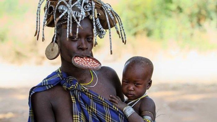 Omo Valley, Ethiopia - December 22, 2010: An unidentified woman of the Mursi tribe with traditional ornaments and lip plate in her village with a baby on her arm