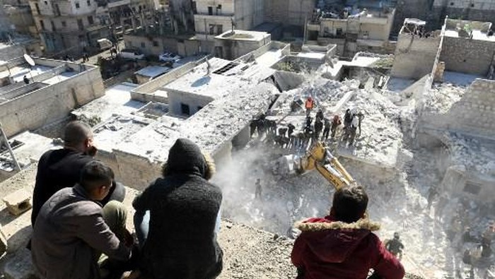 People watch as rescuers sift through the rubble of a building that collapsed in the the northern Syrian city of Aleppo, on January 22, 2023. - The building collapsed today, killing at least 16 people including children, authorities and media reported. (Photo by AFP)