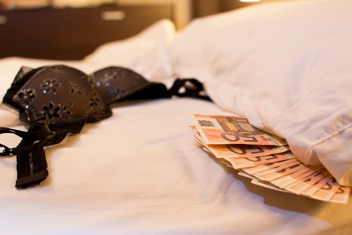 Escort or paid woman lying on bed in brothel. Man paying money for sex worker at night. Hooker with customer. Sexy lady with sugar daddy. Prostitution concept. Private striptease show.