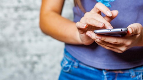 young teenager girl hand using mobile phone or smartphone on gray wall background